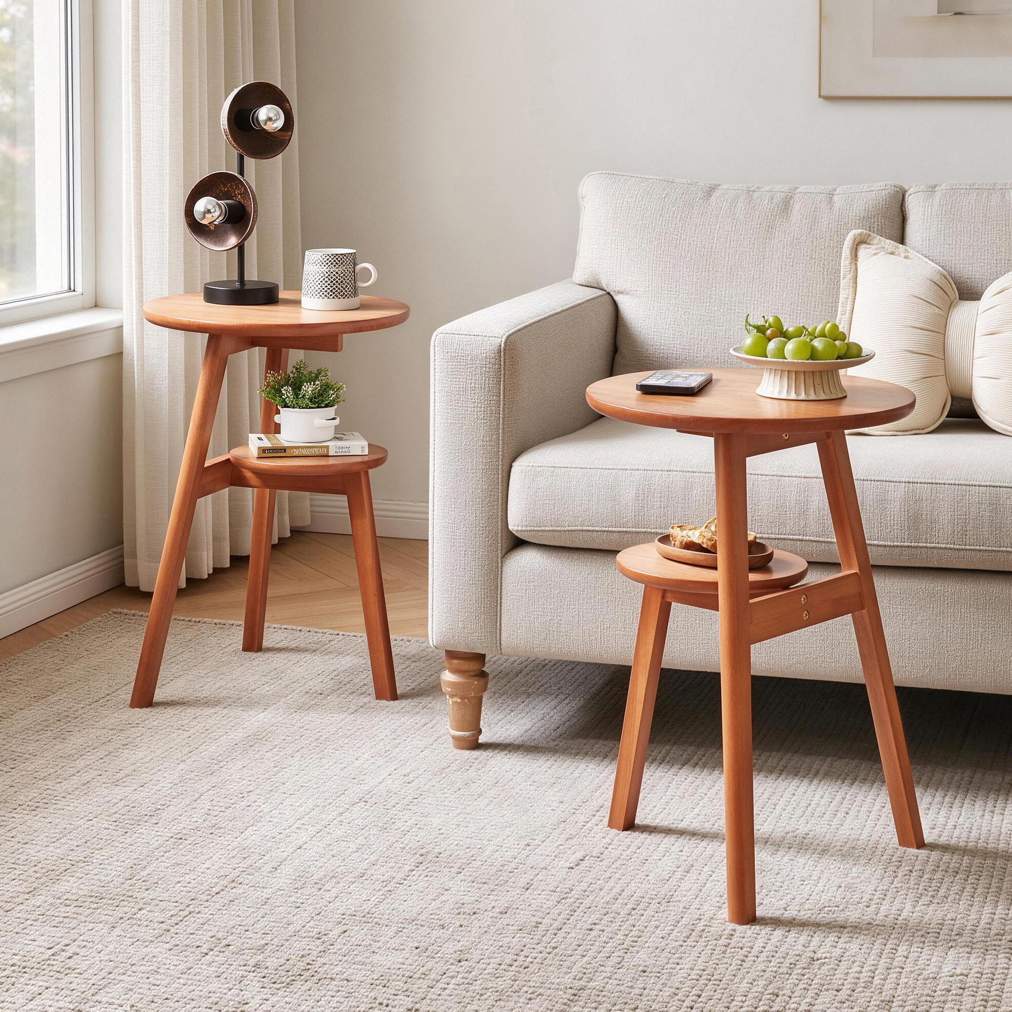Pair of cherry 2-tier round side tables at two heights beside a gray sofa, styled with a speaker, mugs and a fruit bowl