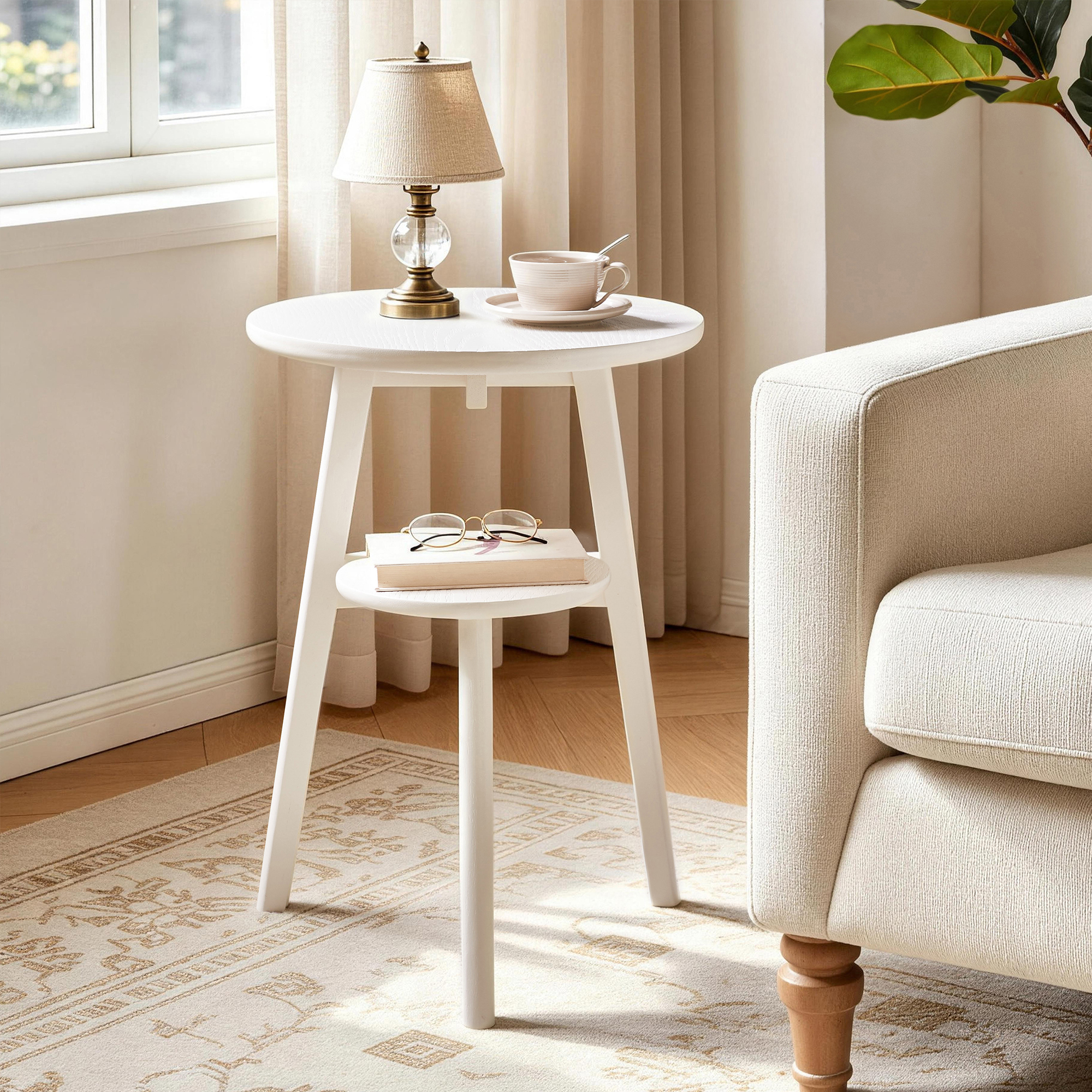 White 2-tier round side table beside an armchair with a table lamp and teacup on top