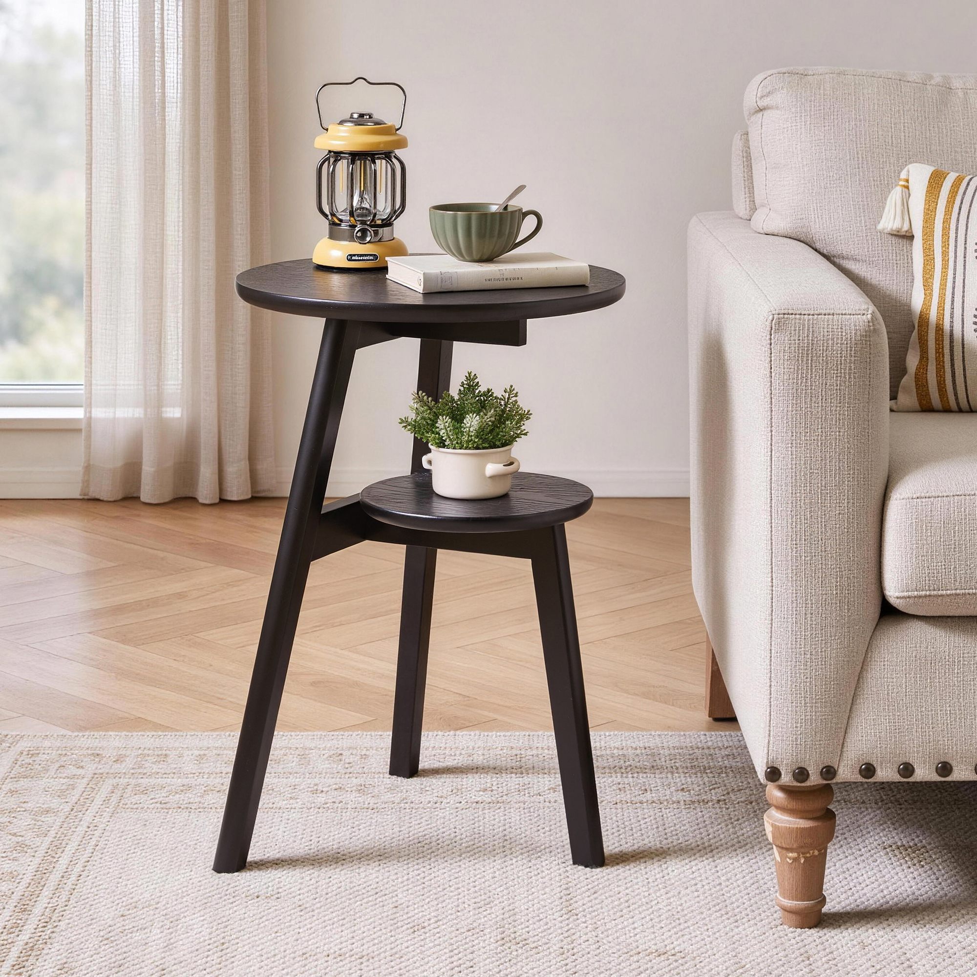 Black 2-tier round side table beside a cream sofa with a lantern and plant on top