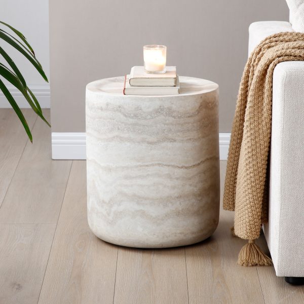 Travertine-look cylinder side table with a candle and books beside a sofa in a warm neutral living room