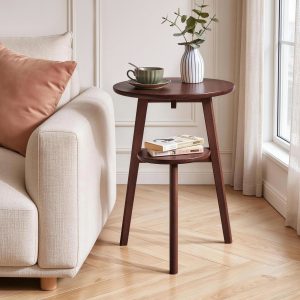 Orivane walnut 2-tier round side table beside a cream sofa in a bright living room, with books stored on the lower shelf