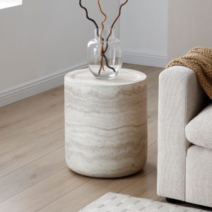 Travertine cylinder side table with a glass vase beside a beige sofa on light wood flooring