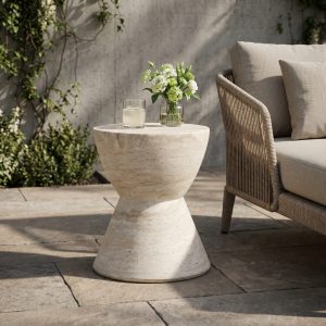 Travertine finish side table beside a woven outdoor armchair on a stone patio with a vase of hydrangeas