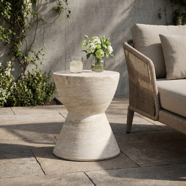 Travertine finish side table beside a woven outdoor armchair on a stone patio with a vase of hydrangeas