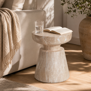 Orivane Ponti travertine side table holding a glass of water and an open book beside a beige sofa in a sunlit living room