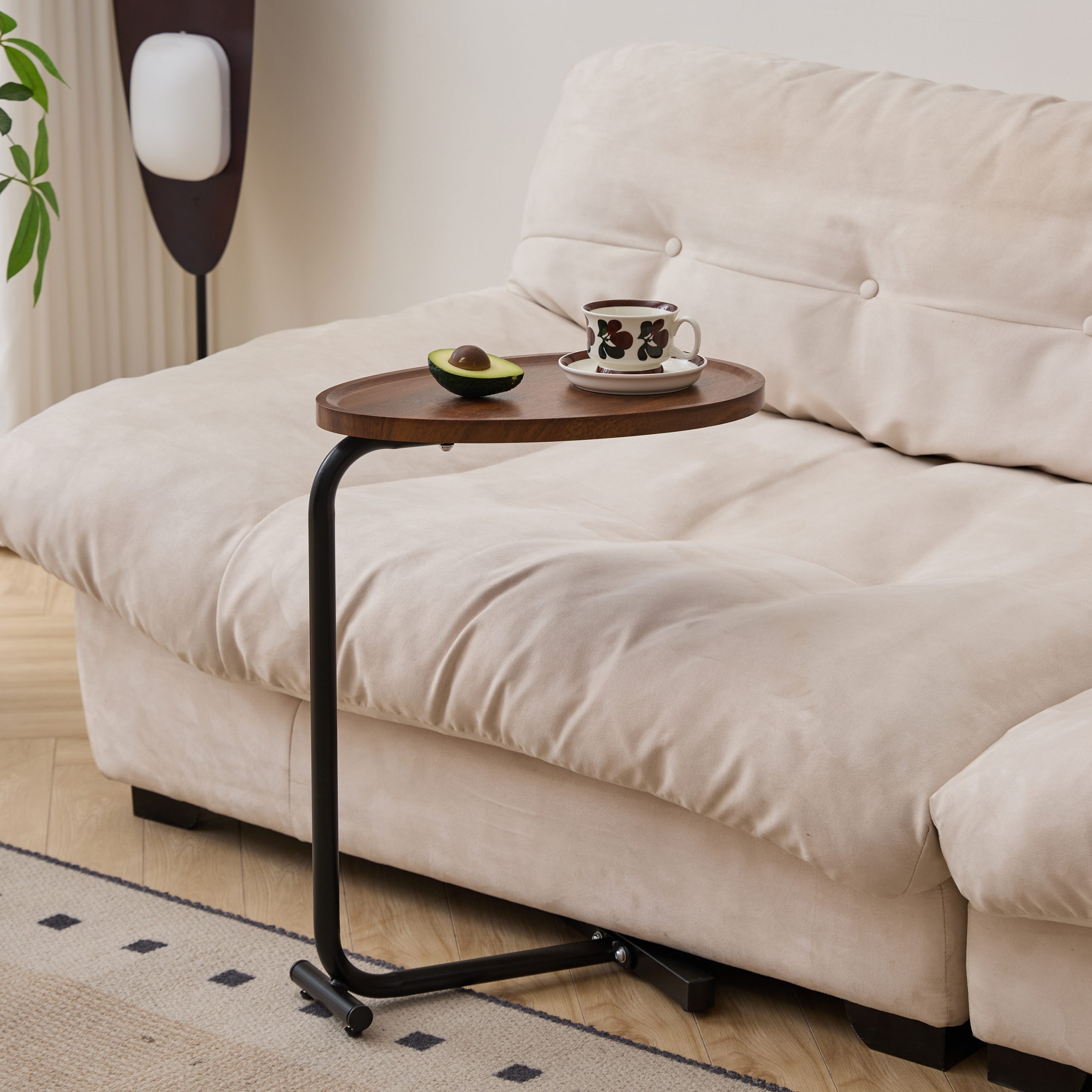 Brown C-shaped sofa table holding a coffee cup and avocado beside a cream sofa