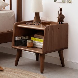 Walnut nightstand with books and camera beside a bed, angled side view