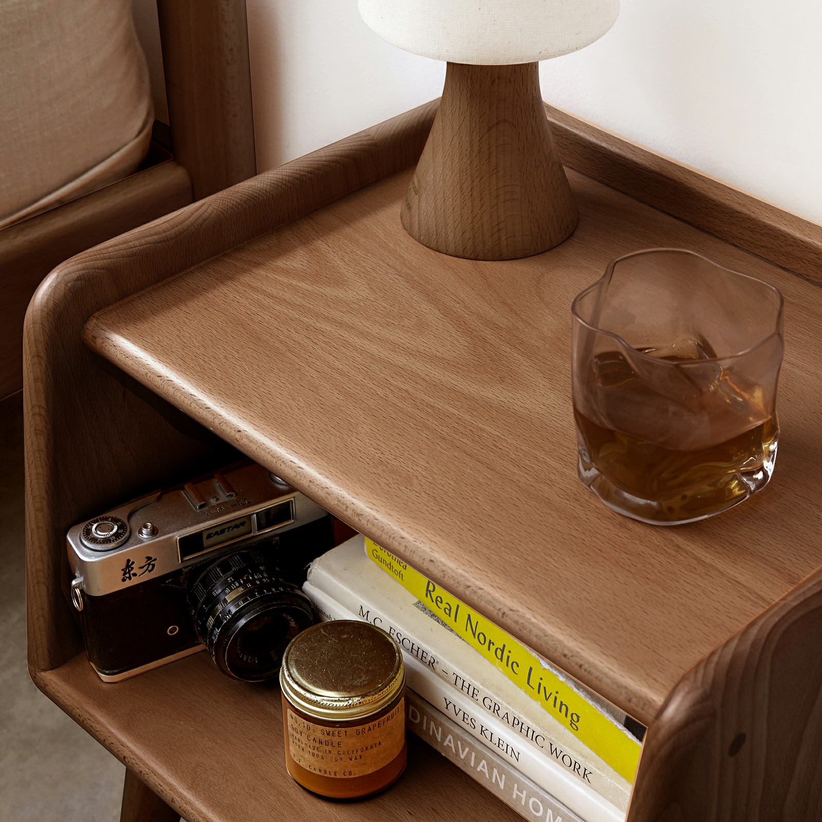 Walnut nightstand with books and camera beside a bed, angled side view